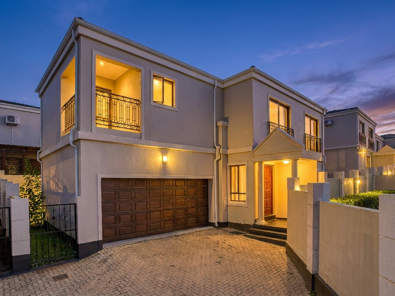 A well-maintained double-storey cluster home featuring a paved driveway, integrated double garage, and an upper-level balcony with wrought iron detailing.