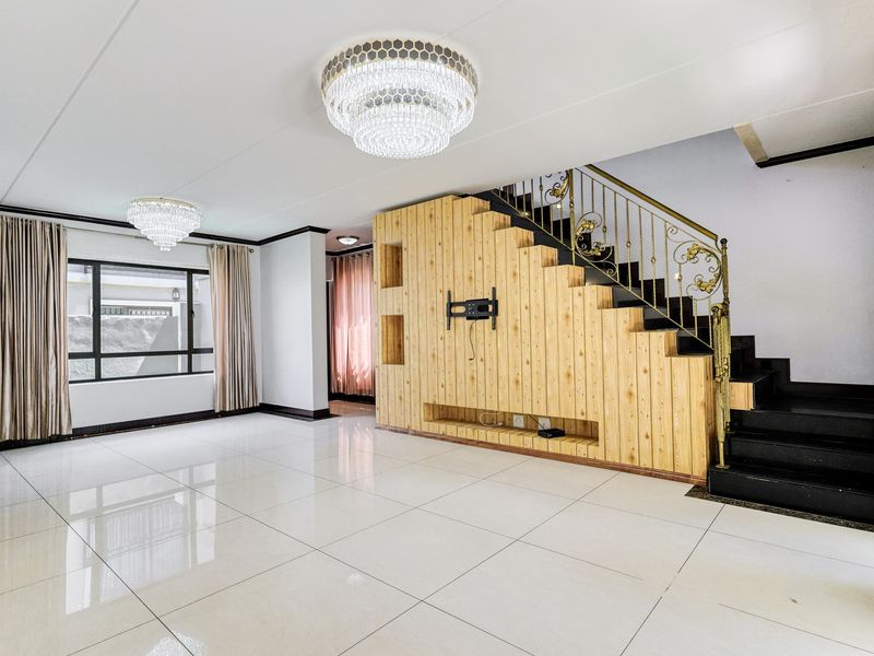 Spacious living area featuring polished porcelain tiles, a custom built-in wooden media wall, and an elegant staircase with decorative metal railings.