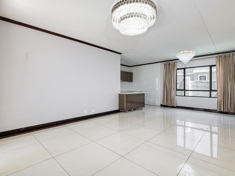 Spacious open-plan living area featuring polished porcelain floor tiles, elegant crystal chandeliers, and a compact built-in kitchen unit with modern cabinetry.
