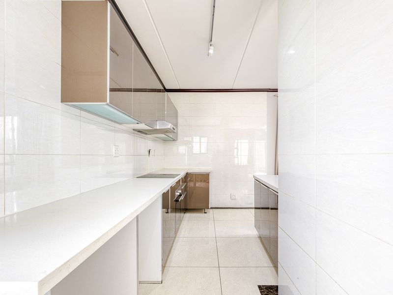 A clean, modern galley-style kitchen featuring high-gloss cabinetry, stone countertops, and full-height wall tiling, presenting a bright and functional workspace.