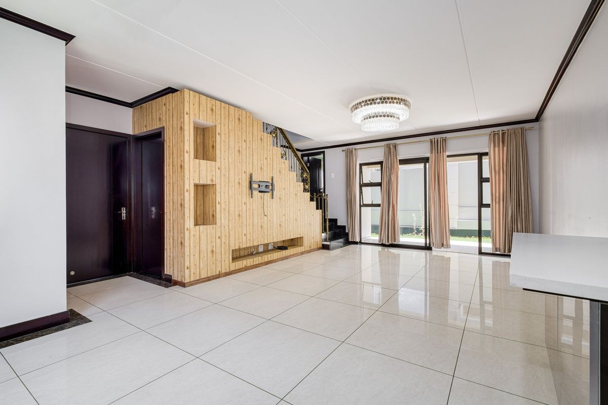 Spacious living area featuring large format floor tiles, a built-in wooden feature wall with integrated shelving, and sliding glass doors leading to the exterior.