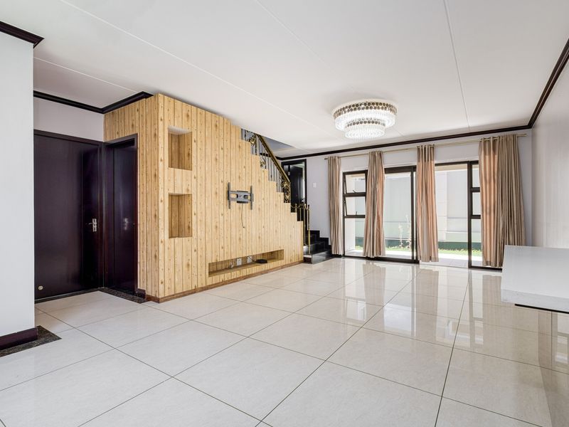 Spacious living area featuring large format floor tiles, a built-in wooden feature wall with integrated shelving, and sliding glass doors leading to the exterior.