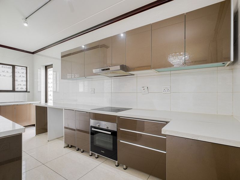 Modern kitchen featuring high-gloss cabinetry, stone countertops, built-in oven, electric hob, and extractor fan, complemented by neutral tiled flooring and backsplash.