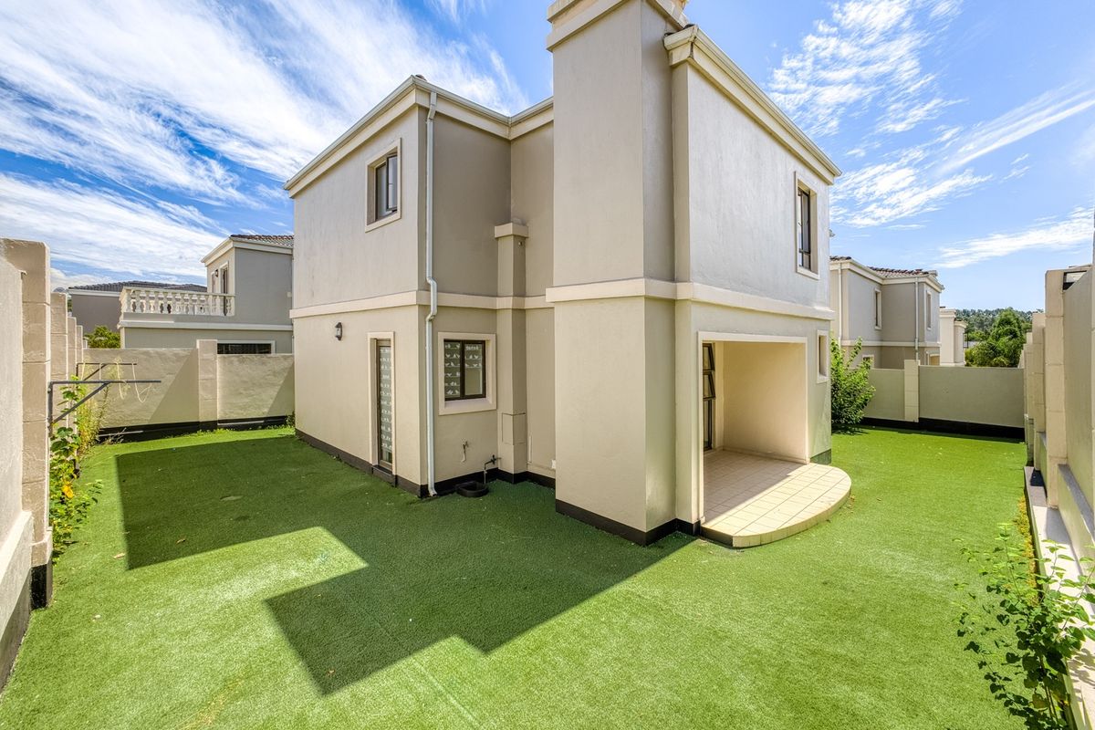 Rear view of the cluster home featuring a covered patio, low-maintenance artificial lawn, and secure boundary walls.