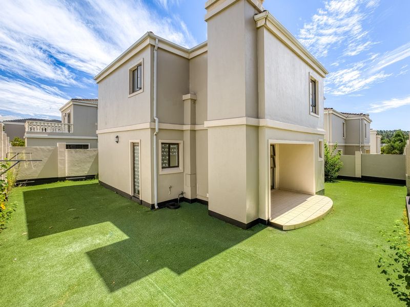 Rear view of the cluster home featuring a covered patio, low-maintenance artificial lawn, and secure boundary walls.