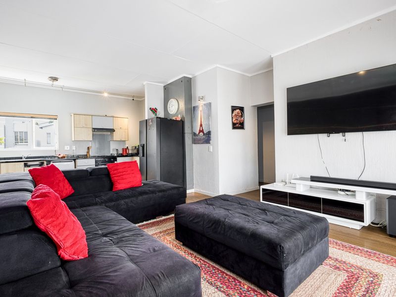 Open-plan living area featuring a modern kitchen with built-in cabinetry and appliances, seamlessly flowing into a spacious lounge area with laminate flooring.