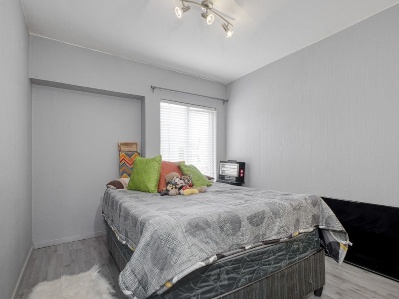 A compact bedroom featuring light grey walls, laminate flooring, and a window fitted with venetian blinds.