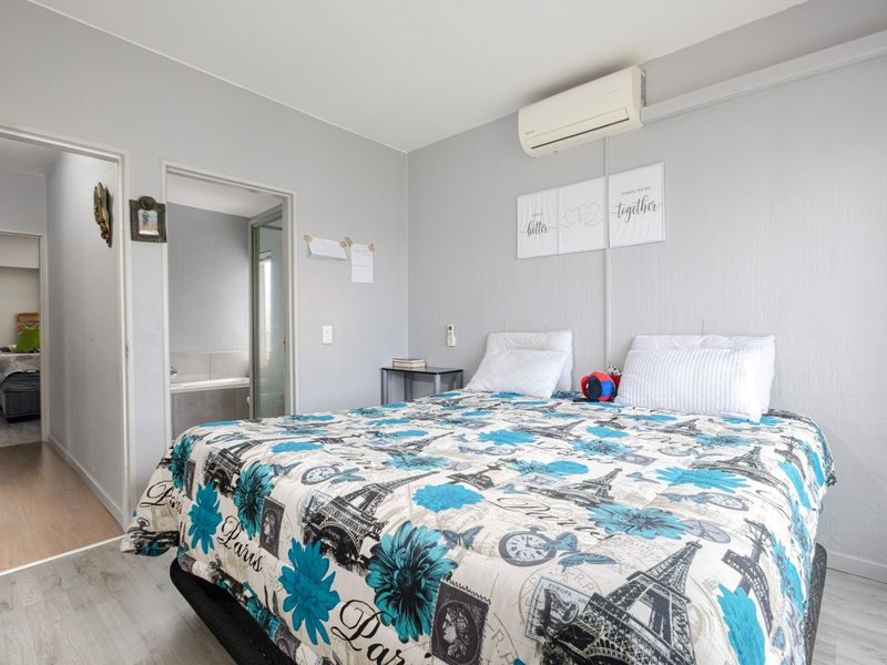 A bedroom featuring light-toned laminate flooring, a wall-mounted split-system air conditioner, and direct access to an adjoining bathroom.