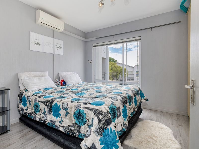 A bedroom featuring laminate flooring, a split-system air conditioner, and a large sliding window providing natural light.