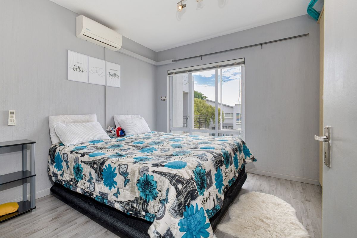 A bedroom featuring laminate flooring, a split-system air conditioner, and a large sliding window providing natural light.