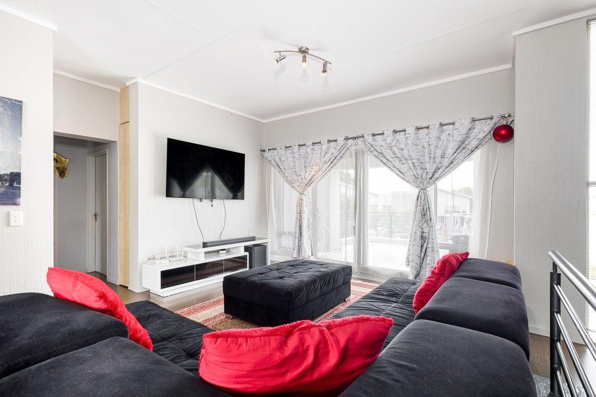 A bright and spacious living room featuring laminate flooring and large sliding glass doors that provide access to an outdoor balcony area.