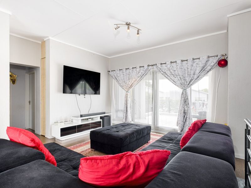 A bright and spacious living room featuring laminate flooring and large sliding glass doors that provide access to an outdoor balcony area.