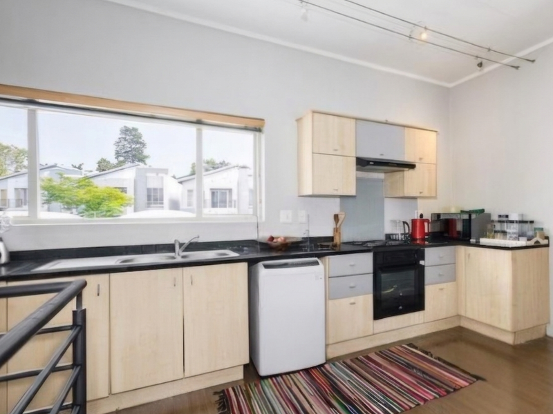 A functional kitchen featuring light wood cabinetry, dark countertops, built-in oven, gas hob, and an extractor fan with large window views.