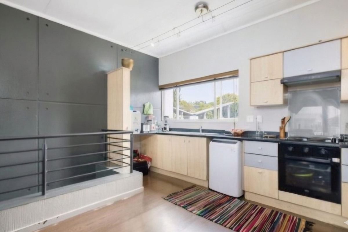 A functional kitchen featuring light wood cabinetry, built-in oven with extractor, and a unique grey feature wall with an adjacent metal balustrade.