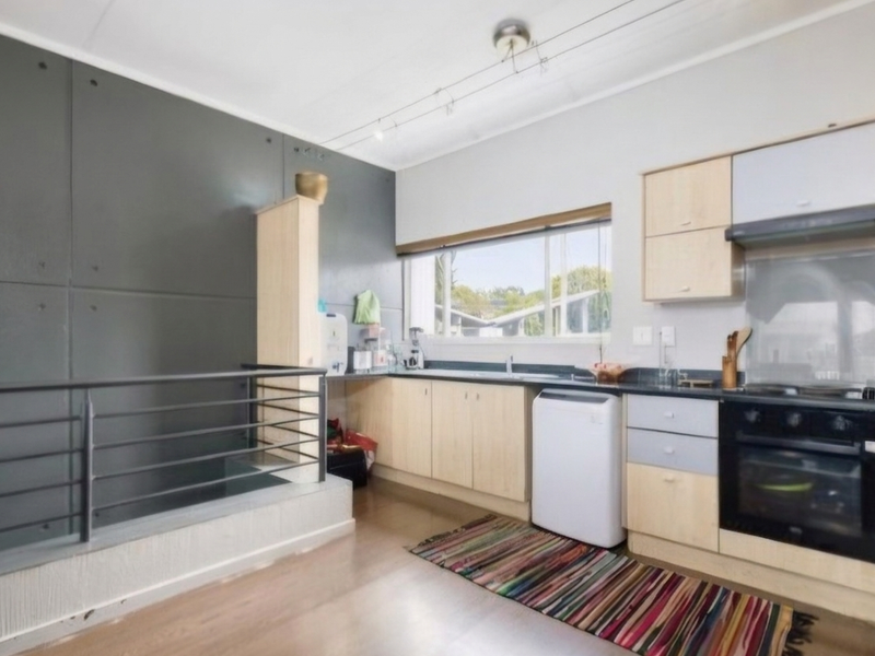 A functional kitchen featuring light wood cabinetry, built-in oven with extractor, and a unique grey feature wall with an adjacent metal balustrade.
