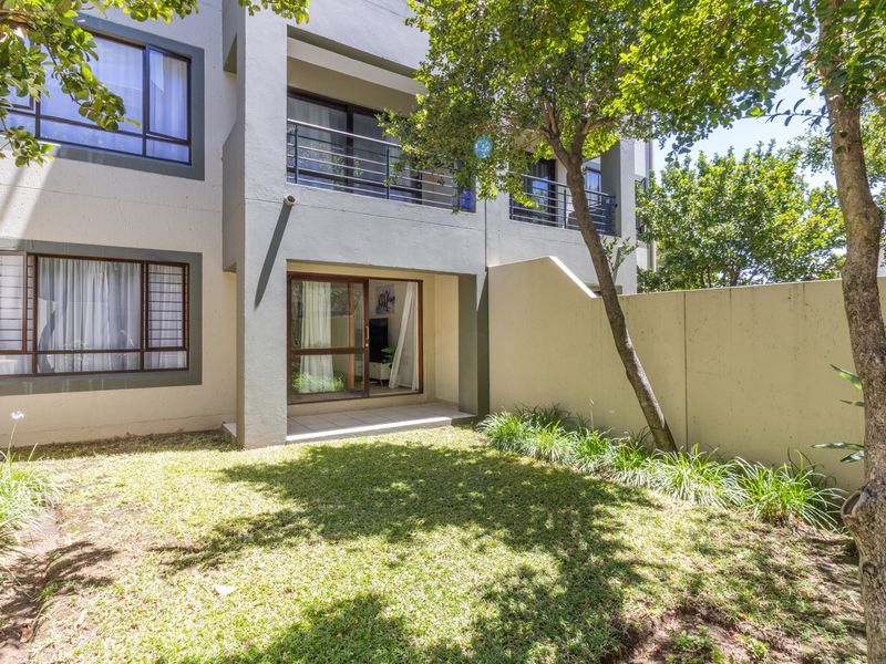 Rear view of the apartment building featuring a private ground-floor patio, sliding door access, and a small enclosed garden area.