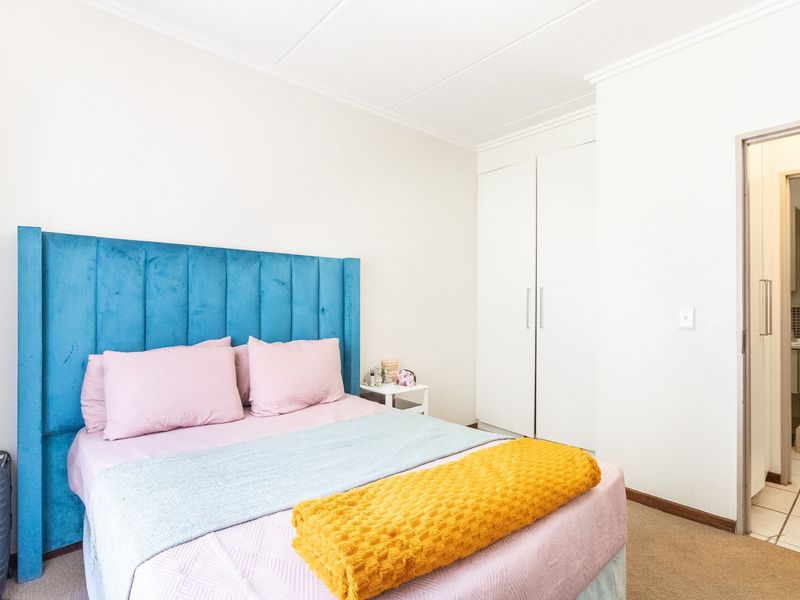 A well-maintained bedroom featuring neutral walls, built-in cupboards, and carpeted flooring, with an adjoining doorway leading to an en-suite bathroom.
