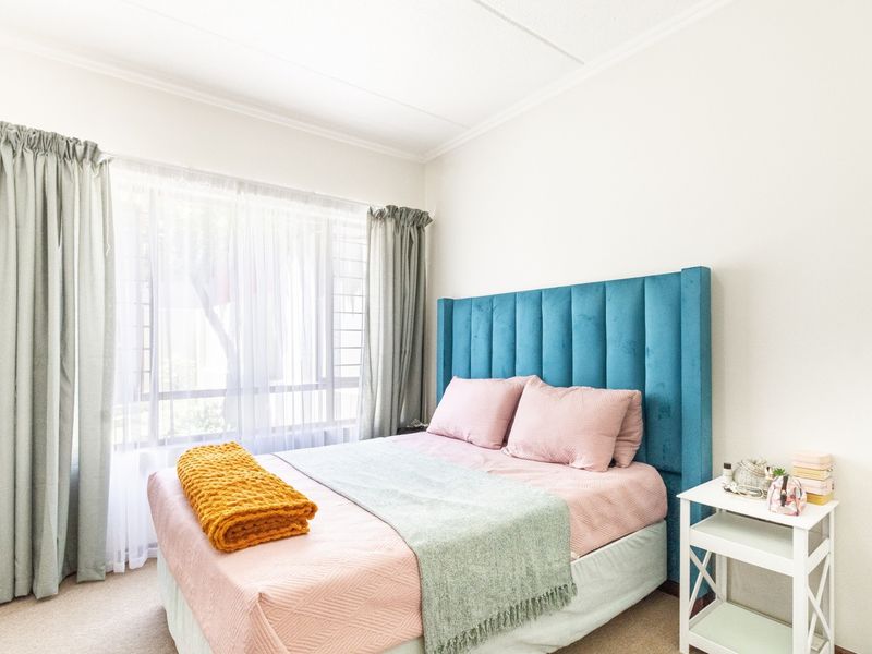 A bright and well-lit bedroom featuring neutral carpeting, a large window with natural light, and classic ceiling cornice detailing.