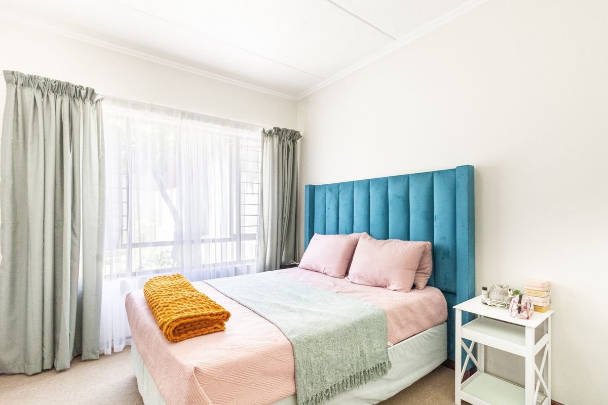 A bright and well-lit bedroom featuring neutral carpeting, a large window with natural light, and classic ceiling cornice detailing.