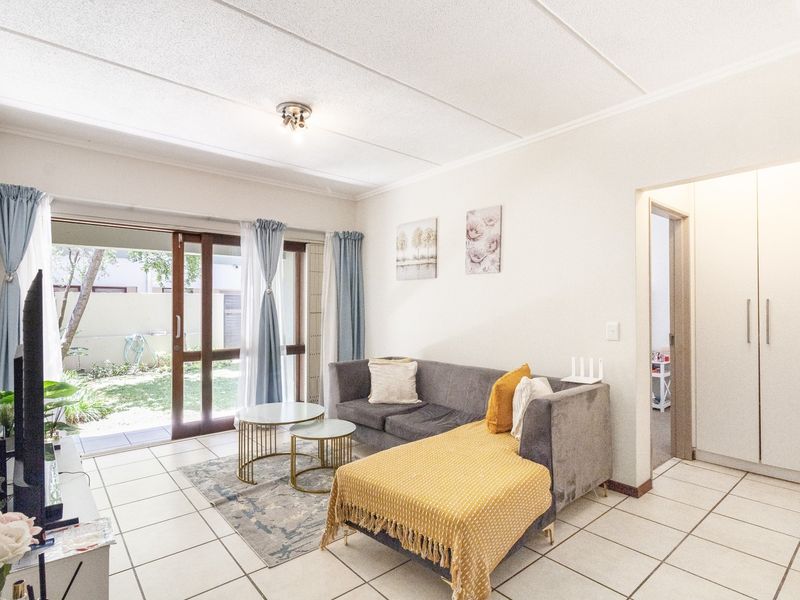 Bright living room featuring tiled flooring, built-in storage cupboards, and a sliding glass door providing direct access to the outdoor garden area.