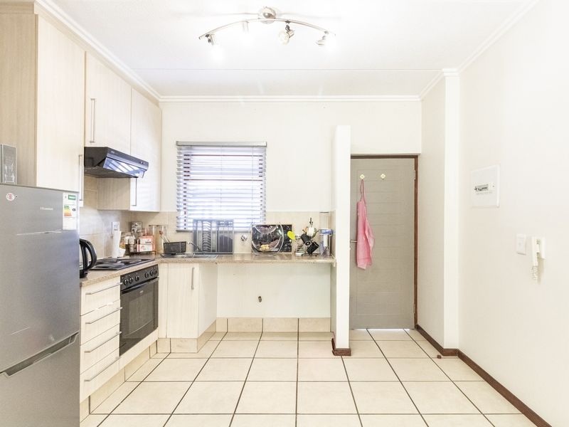 A functional kitchen featuring light-toned cabinetry, built-in oven and hob, tiled flooring, and a window with venetian blinds.