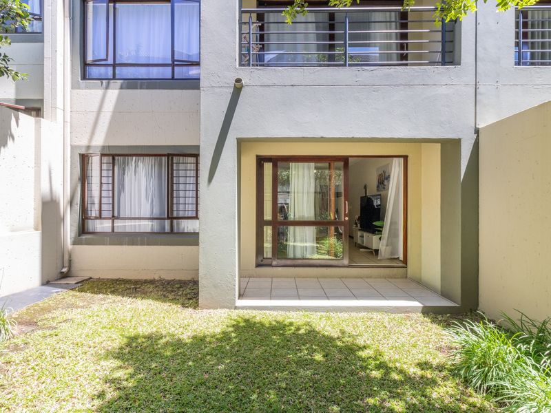 Rear view of the apartment featuring a small tiled patio, a sliding glass door entrance, and a private lawn area.