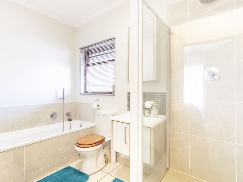 A bright, modern bathroom featuring a built-in bathtub, a separate glass-enclosed shower, a vanity unit, and neutral floor-to-ceiling tiling.