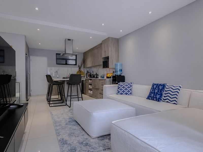 Modern open-plan living area featuring a sleek kitchen with built-in cabinetry, a central island, and high-quality tiled flooring throughout the space.