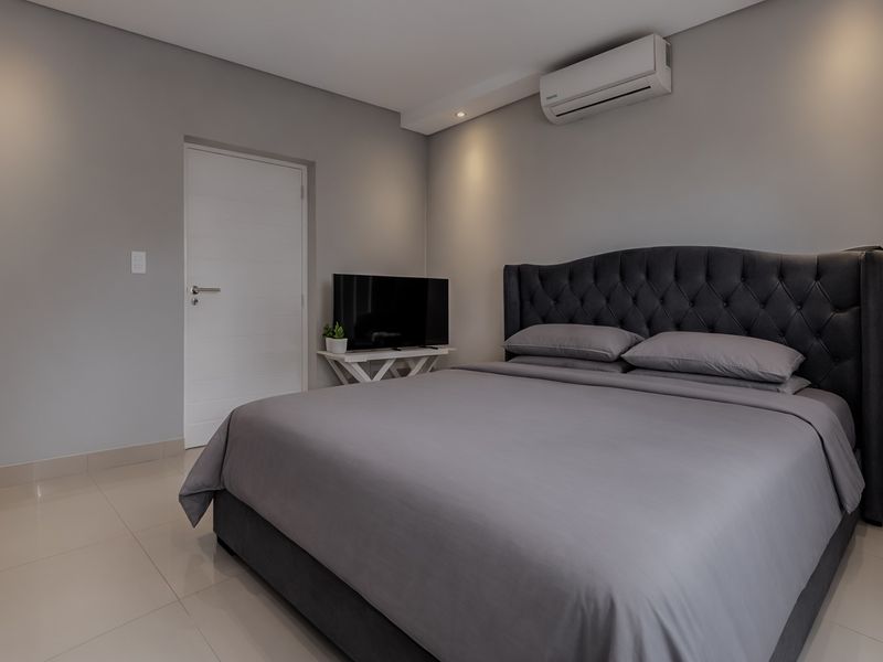 A modern, well-maintained bedroom featuring neutral grey walls, tiled flooring, recessed lighting, and a wall-mounted split-system air conditioning unit.
