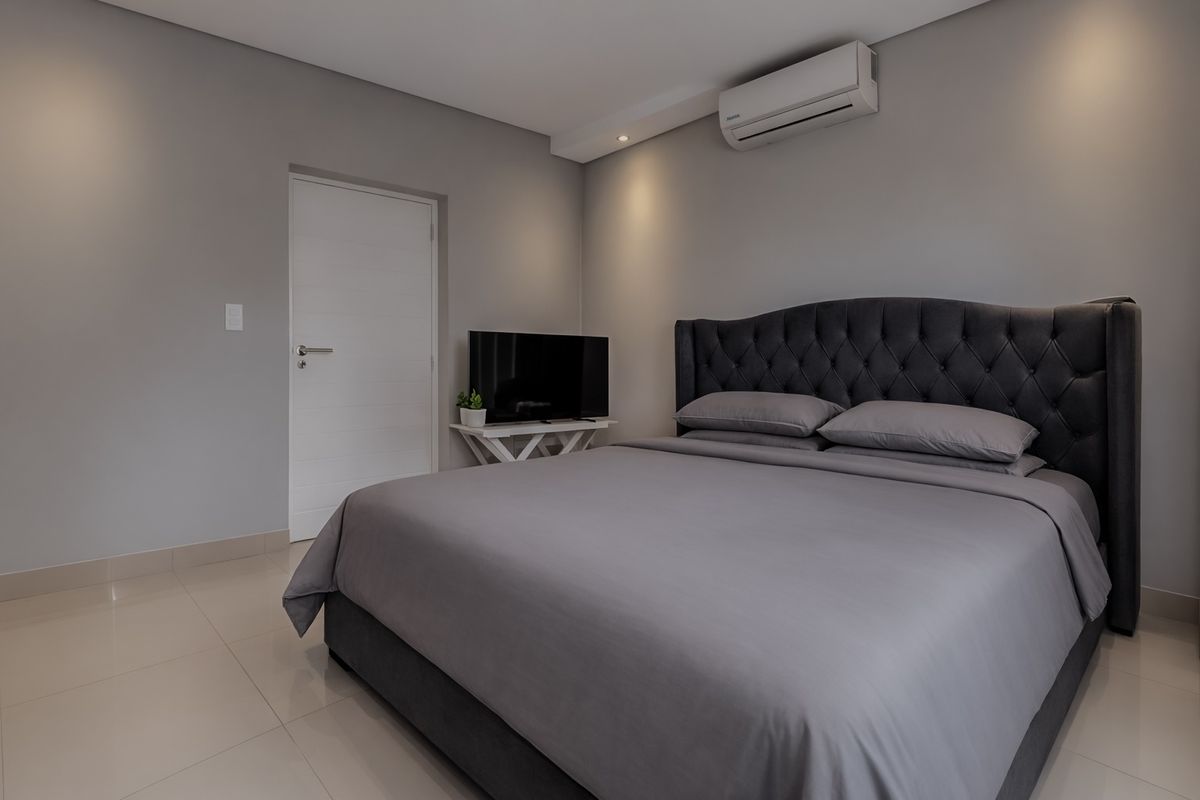 A modern, well-maintained bedroom featuring neutral grey walls, tiled flooring, recessed lighting, and a wall-mounted split-system air conditioning unit.