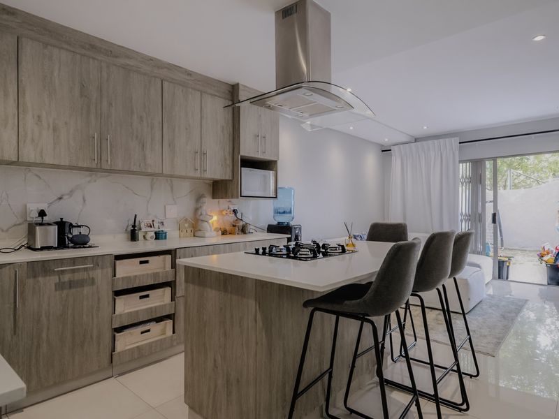 Modern open-plan kitchen featuring wood-grain cabinetry, stone countertops, a central island with a gas hob, and direct access to an outdoor patio area.