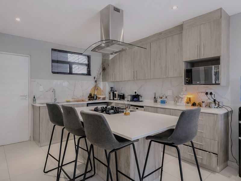 Modern kitchen featuring a central island with a gas hob, sleek laminate cabinetry, marble-look splashback, and integrated appliances.