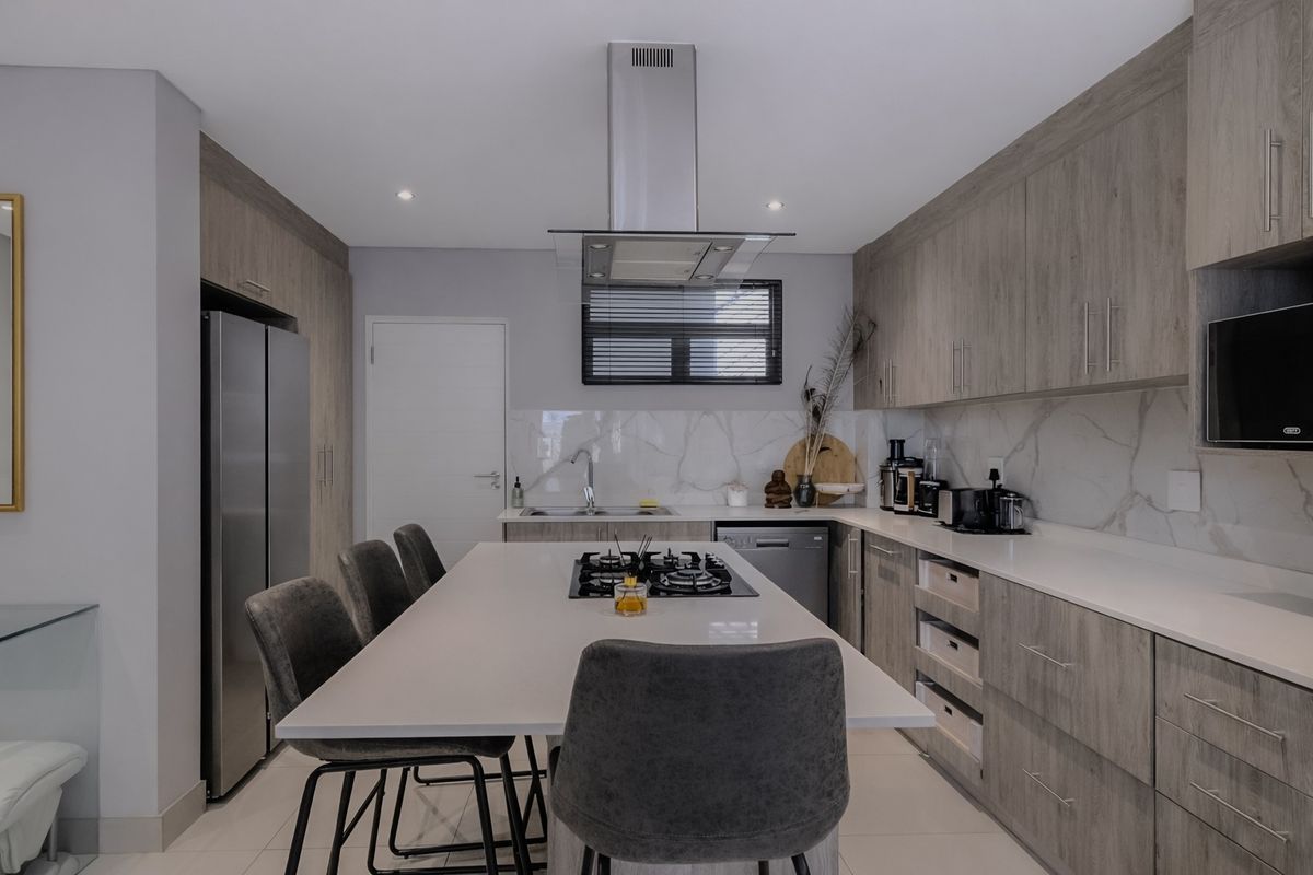 Modern kitchen featuring wood-grain cabinetry, stone countertops, a central island with a gas hob, and high-end integrated appliances.