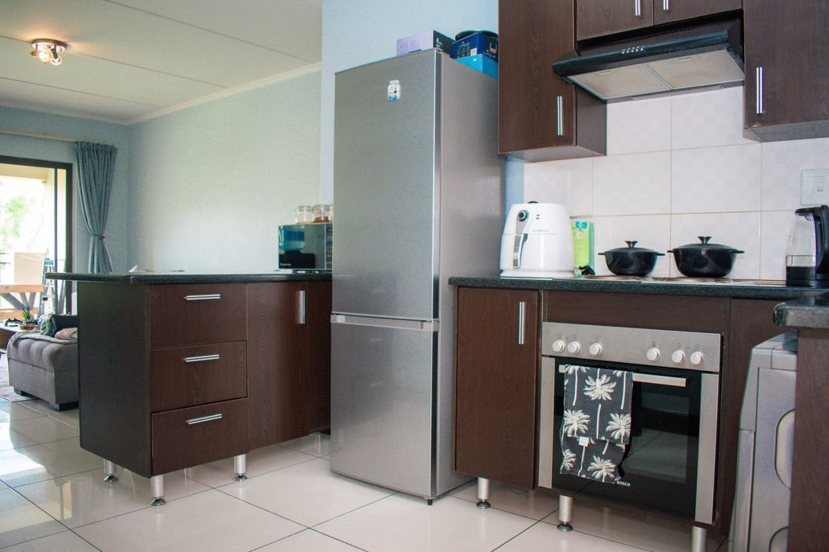 A functional kitchen featuring dark wood cabinetry, granite countertops, built-in oven, extractor fan, and tiled flooring, seamlessly connected to the living area.
