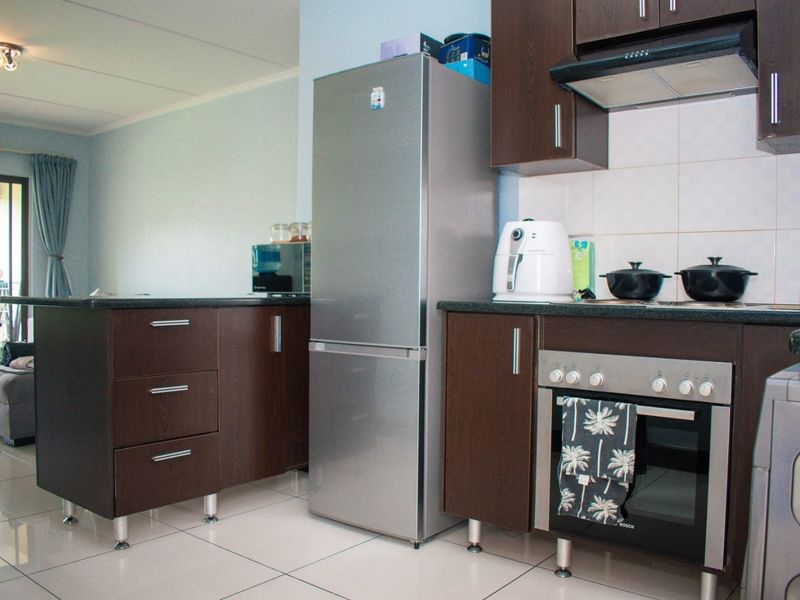 A functional kitchen featuring dark wood cabinetry, granite countertops, built-in oven, extractor fan, and tiled flooring, seamlessly connected to the living area.