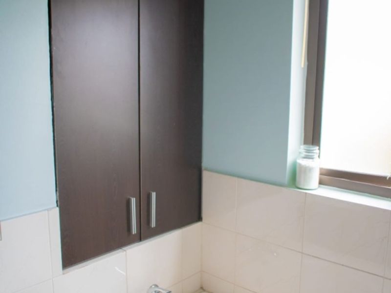 A functional bathroom featuring a built-in bathtub with chrome fixtures, tiled splashbacks, and a dark wood-finish wall cabinet for storage.