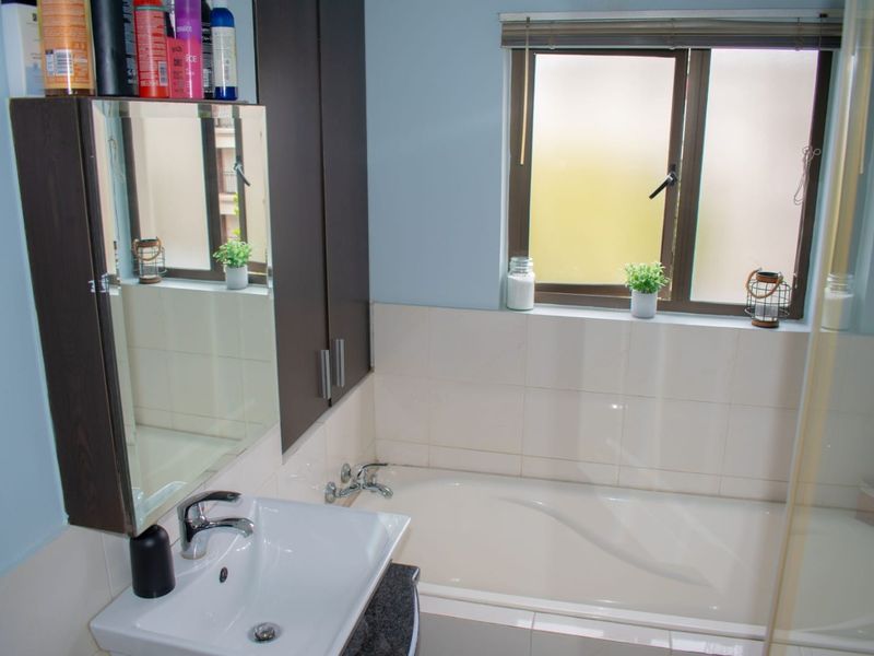 A functional bathroom featuring a built-in bathtub, vanity cabinet with integrated mirror, and tiled splashback, providing a practical space with natural light.