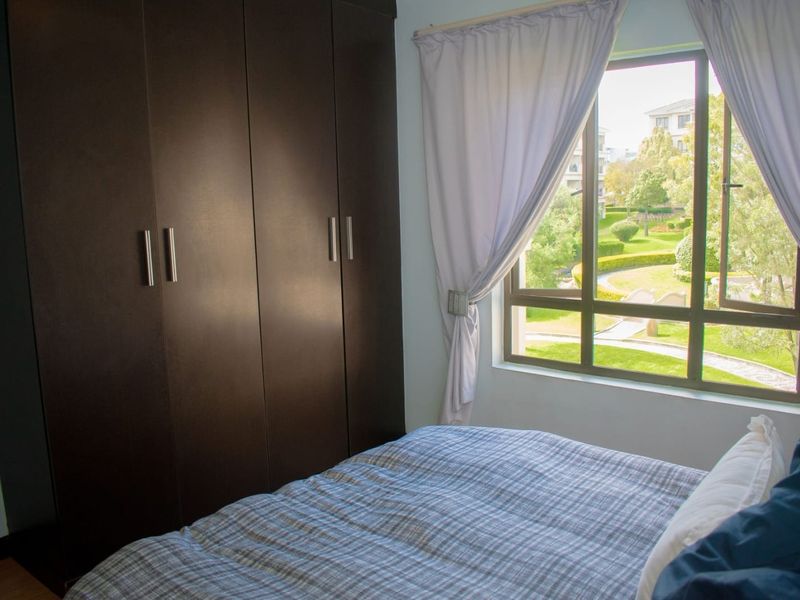 A bedroom featuring dark wood built-in cupboards and a window with views of the landscaped garden area.
