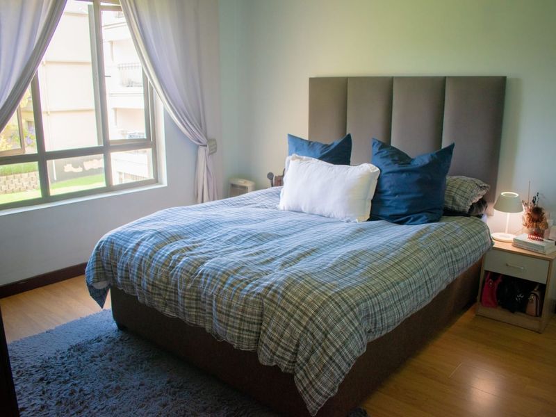 A well-lit bedroom featuring laminate flooring and a large window providing natural light.