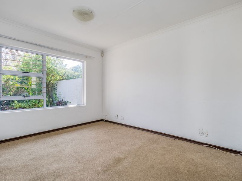 An empty bedroom featuring neutral walls, carpeted flooring, and a large window overlooking the garden area.
