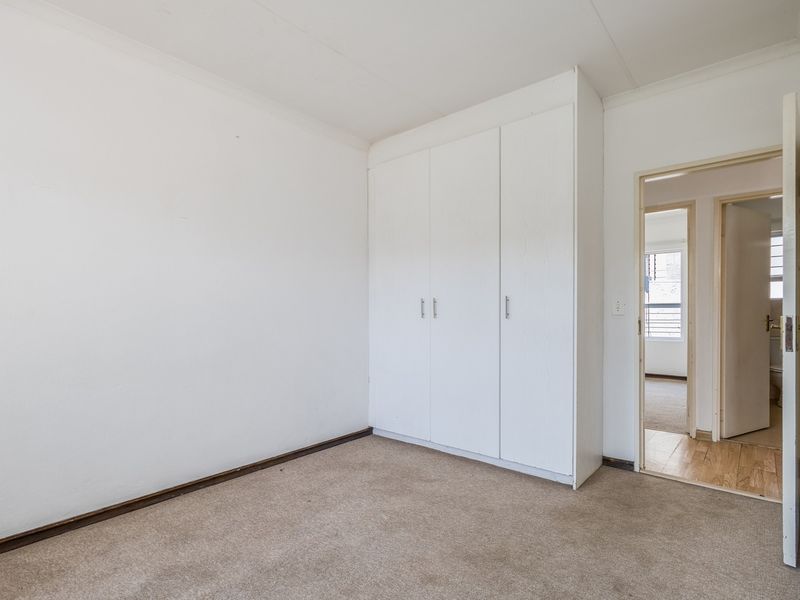 An empty bedroom featuring built-in cupboards, neutral walls, and carpeted flooring, with a doorway leading to an adjacent room.
