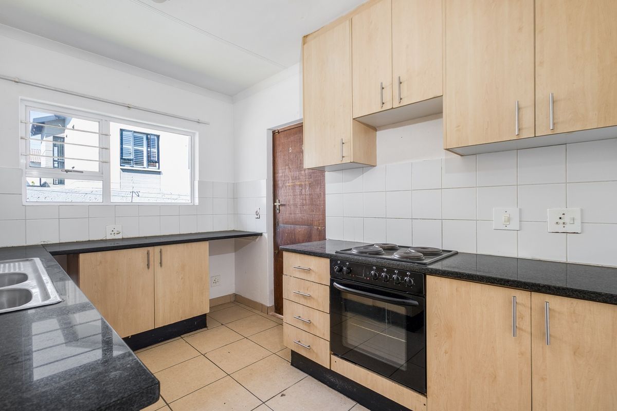 A functional kitchen featuring light wood cabinetry, granite countertops, a built-in oven and hob, and tiled flooring.