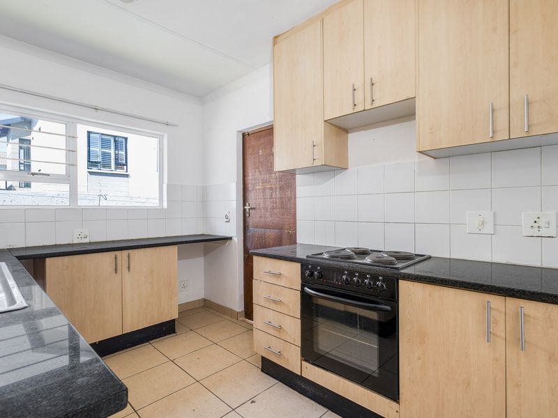 A functional kitchen featuring light wood cabinetry, granite countertops, a built-in oven and hob, and tiled flooring.