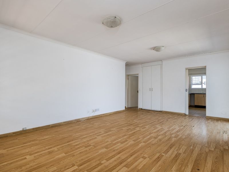 A spacious, empty living area featuring laminate flooring, neutral walls, and a built-in cupboard, with direct access to an adjacent kitchen area.