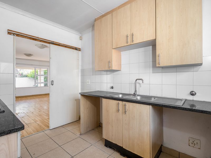 A functional kitchen featuring laminate cabinetry, granite countertops, and a double bowl sink, with an adjacent room visible through a sliding door.