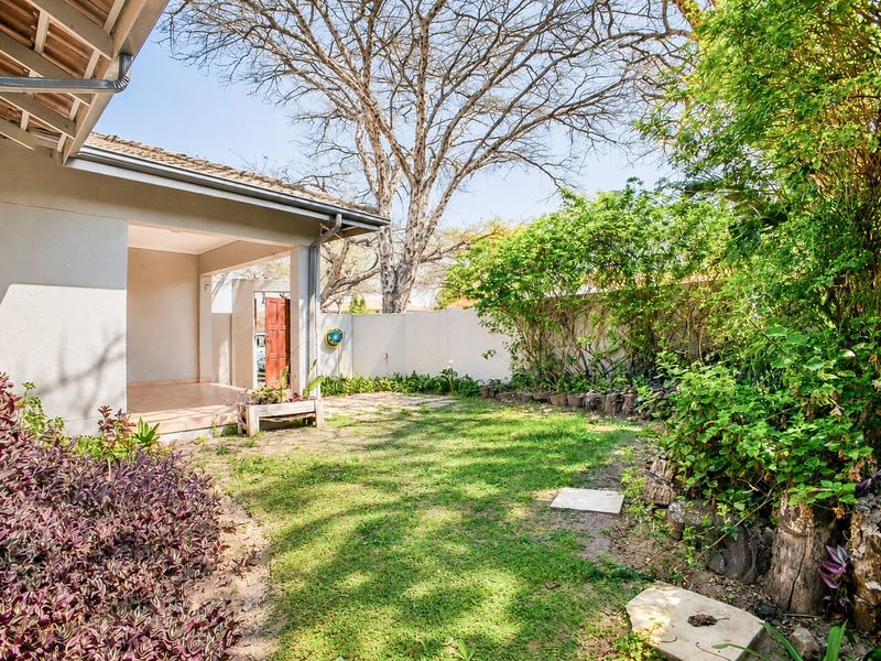 A private rear garden featuring a covered patio area, established landscaping, and a boundary wall, providing a quiet outdoor space for the townhouse.