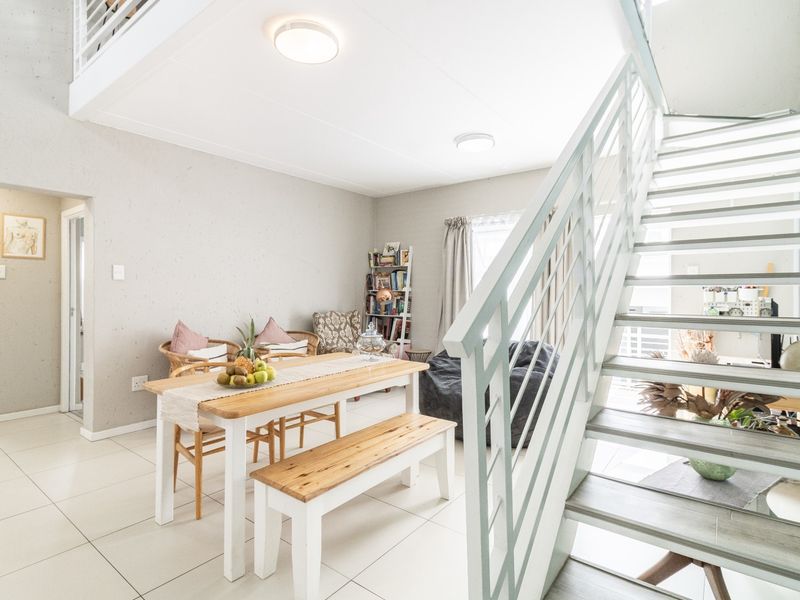 Open plan living and dining area featuring a modern staircase with metal balustrade, tiled flooring, and a mezzanine level above.