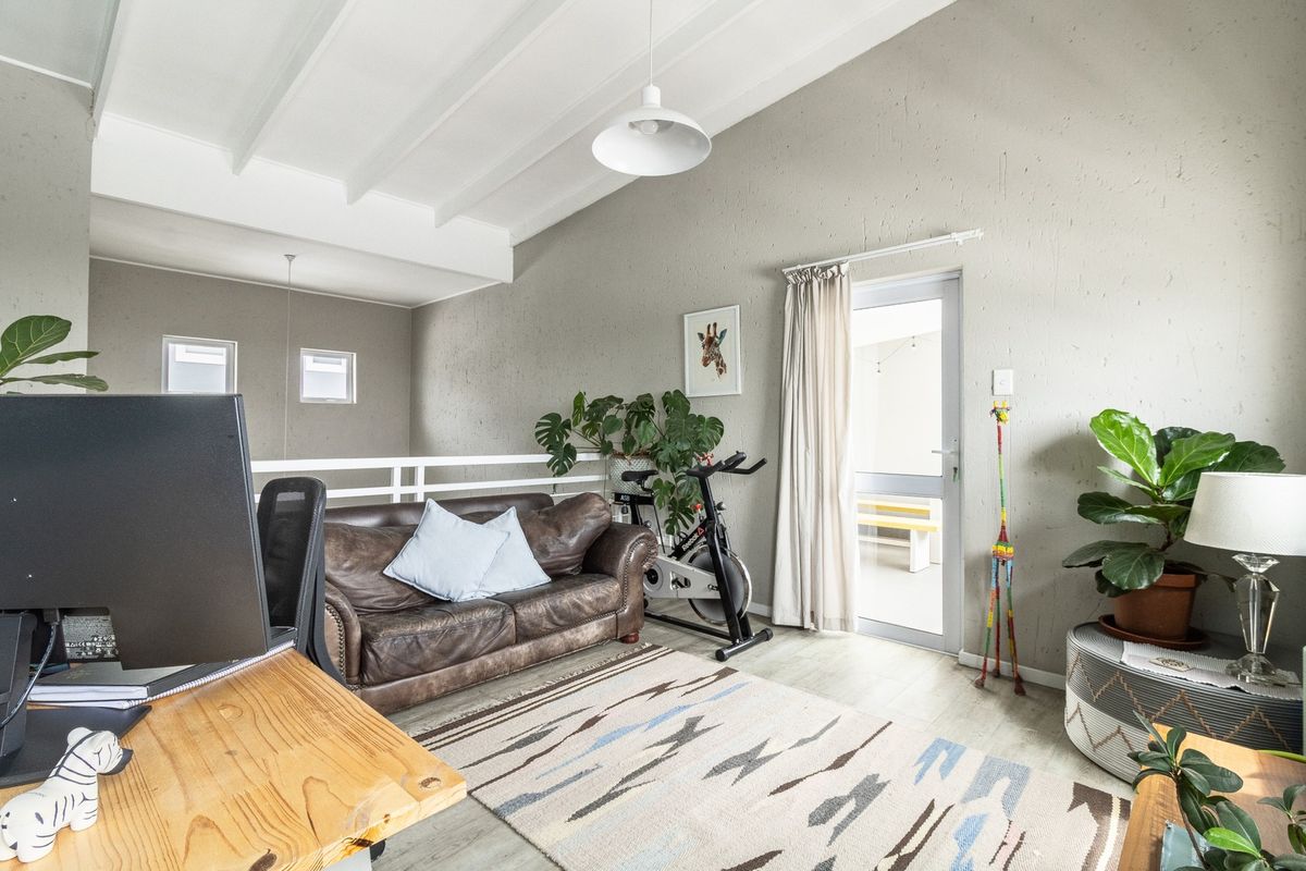 Spacious living area featuring a vaulted ceiling with exposed beams, laminate flooring, and direct access to an outdoor patio through a glass panel door.