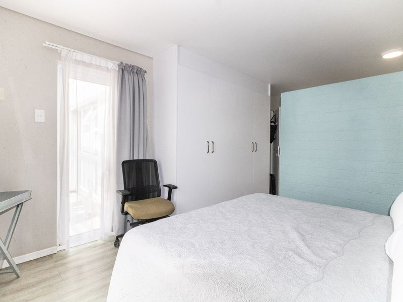 A bright bedroom featuring built-in cupboards, light laminate flooring, and a glass door providing access to an outdoor area.