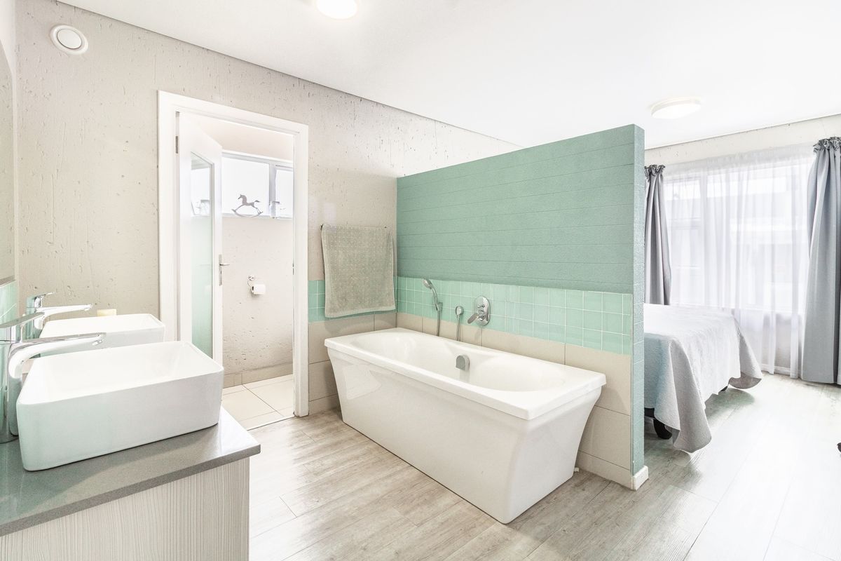 Modern open-plan bathroom featuring a freestanding bathtub, double vanity with contemporary basins, and a stylish partition wall with tiled splashback.